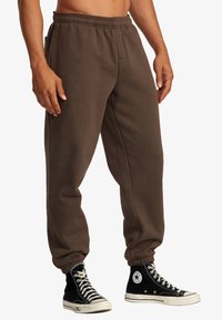 Braune Sweatpants mit elastischem Bund, Bündchen an den Knöcheln und seitlichen Taschen. Kombiniert mit schwarzen High-Top-Sneakern.
