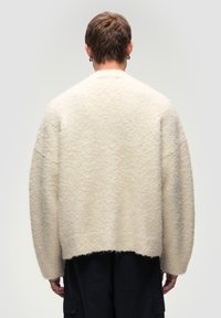 Maglione oversize color crema con un knit texturizzato e fluffy. Presenta spalle a caduta e un orlo dritto, realizzato in un materiale caldo e morbido.