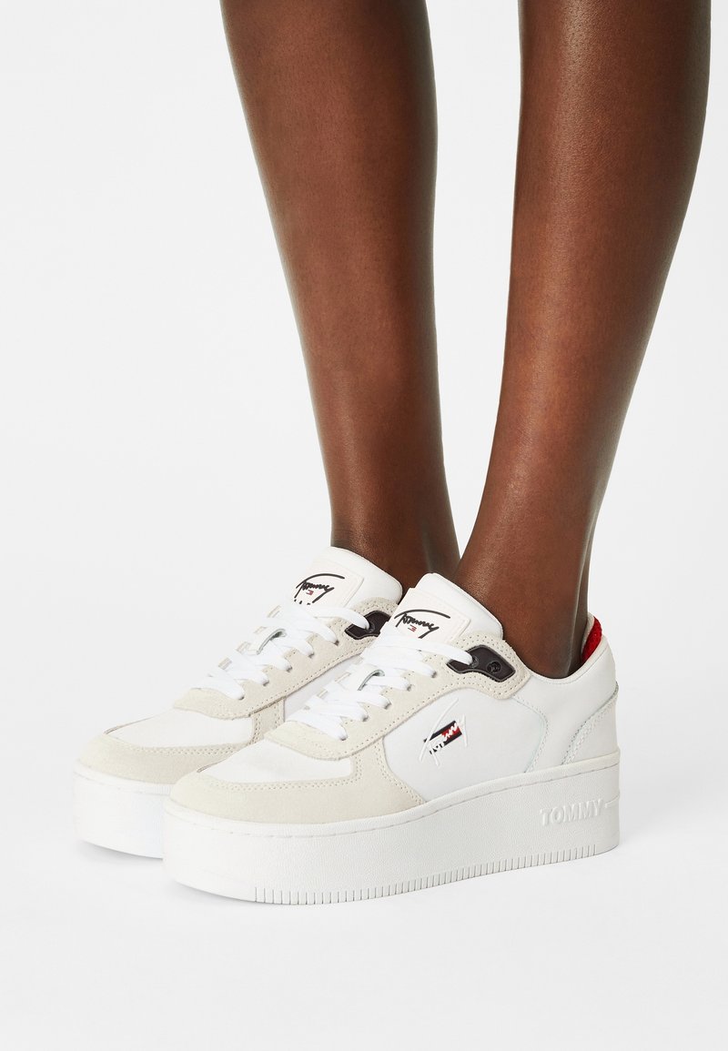 Personne portant des baskets à plateforme blanches avec des accents beiges, des lacets et le logo Tommy sur le côté et la languette.