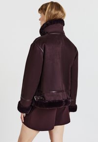 Bordeauxrote Lammfelljacke mit hohem Kragen, Lederakzenten und mit Fell gefütterten Bündchen. Verfügt über eine Schnallendetail am Taillenbereich und einen lockeren Schnitt.