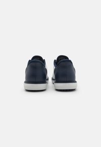 Baskets en cuir navy avec semelles en caoutchouc blanc, talons arrondis et design minimaliste. Présentent des accents texturés et des détails de marque au niveau du talon.