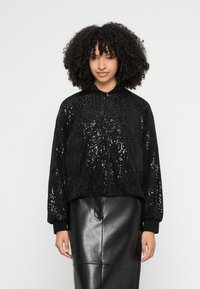 Juoda bombonešio striukė, padengta juodomis blizgučiais, su priekyje esančia užtrauktuku ir austo audinio rankogaliais. Dėvima su juoda odine sijonu.