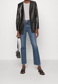 Musta nahkatakki, jossa on ryhdikäs muotoilu, harmaa t-paita, korkeavyötäröiset siniset farkut ja mustat korkokengät. Pieni musta olkalaukku.