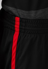 Pantalones cortos deportivos negros con una cinturilla texturizada. Presenta una franja roja prominente a lo largo del costado. Tejido suave, material elástico.
