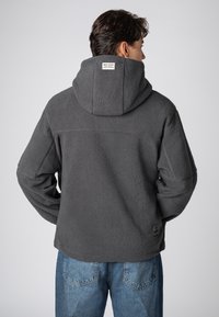 Grau Fleece-Hoodie mit strukturierter Oberfläche, versehen mit einer Kapuze und einem kleinen Markenetikett auf der Rückseite. Kombiniert mit blauen Jeans.