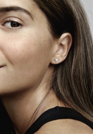 Heart-shaped stud earring in rose gold with small round gemstones accenting the edge, worn on the left ear, against a neutral background.