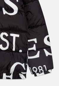 Juoda pūkinė striukė su ryškiu baltu tekstu ir skaičiais, siuvinėjimu, blizgiu audiniu ir elastinėmis rankovėmis.