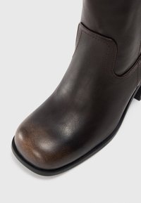 Bottines en cuir marron avec un bout arrondi, présentant une texture subtile et une zone plus claire contrastante sur le bout. Semelle en caoutchouc noire.