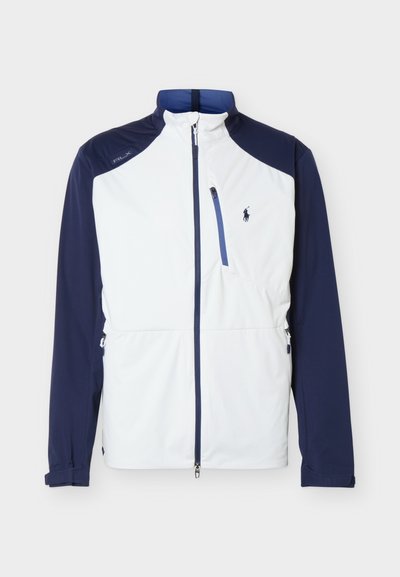 Chaqueta softshell blanca y azul marino con cremallera frontal completa, bolsillo en el pecho con cremallera, mangas largas y pequeño logo azul marino bordado en el pecho izquierdo.