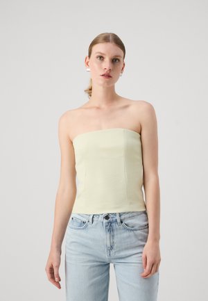 Strapless, light yellow top with a smooth texture and structured form, paired with light blue denim jeans.