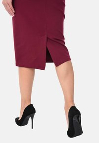 Gonna aderente bordeaux con uno spacco laterale, abbinata a scarpe con tacco alto in suede nero con punta lucida e tacco a stiletto.