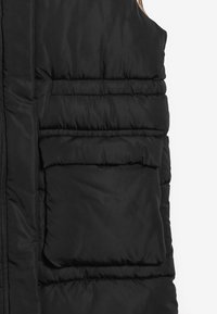 Schwarze Steppweste mit einem quilted Design, ausgestattet mit einem Reißverschluss und zwei Fronttaschen. Glatte Textur mit mattem Finish.