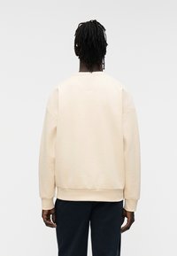 Sweatshirt de couleur crème avec une coupe décontractée, épaules tombantes et poignets côtelés ; texture douce et design simple et classique.