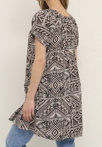 Tunika z krótkim rękawem, wzorzysta w ziemistych odcieniach beżowego i brązowego, z motywami geometrycznymi. Lekka tkanina oraz luźny krój.