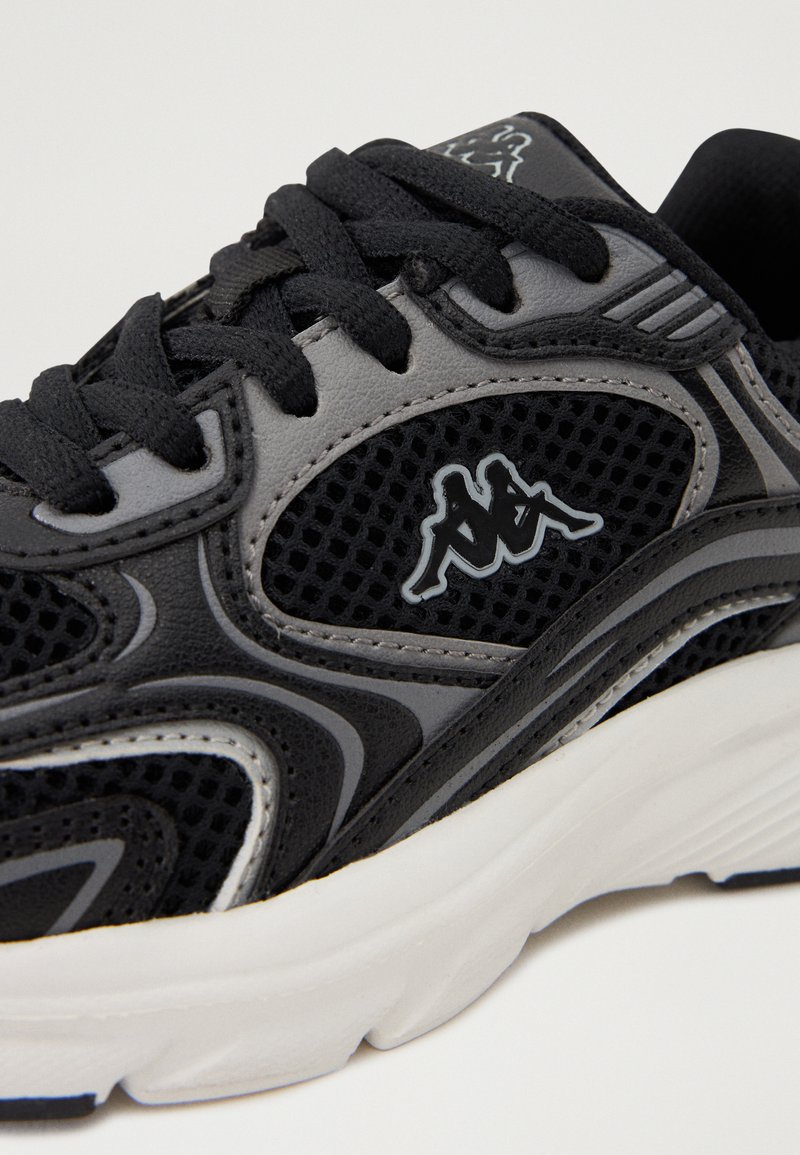 Chaussures de sport noires et grises en matériau mesh et synthétique, avec des accents texturés et un logo bien en vue sur le côté. Semelle blanche.