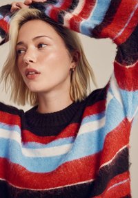 Knit sweater featuring bold stripes in red, blue, and white, with a dark brown base. Ribbed neckline and soft texture.