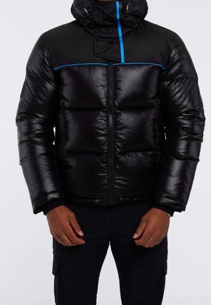 Black puffer jacket with blue trim on shoulders and hood, front zipper, worn by person with dark pants, hands relaxed at sides.