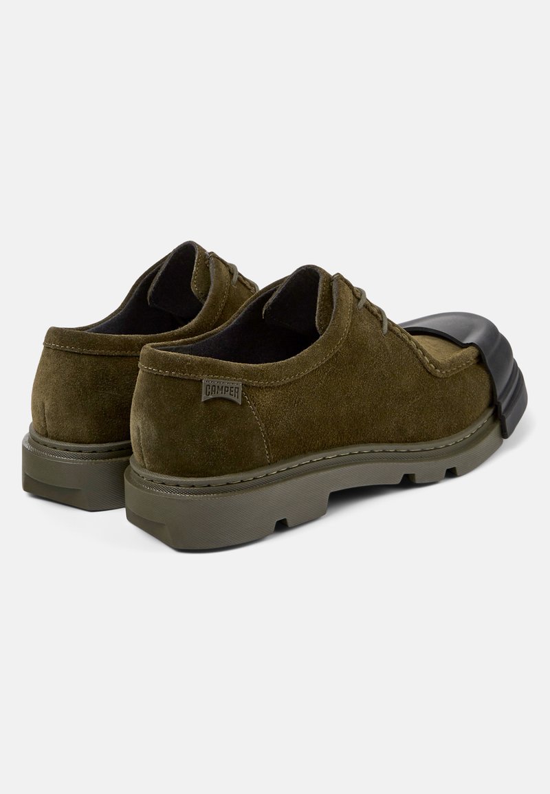 Olivenfarbene Wildlederschuhe mit runder Spitze und schwarzem Gummikäppchen. Ausgestattet mit einer dicken grauen Sohle, Schnürdesign und genähten Details.