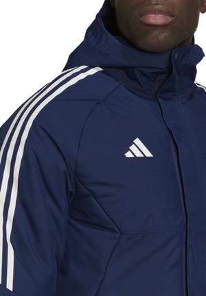 Marineblaue isolierte Jacke mit Kapuze, die weiße Akzentstreifen mit drei Streifen an den Ärmeln und ein weißes Adidas-Logo auf der Brust aufweist.
