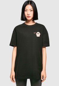 Zwarte katoenen T-shirt met korte mouwen, voorzien van een roze spookafbeelding en de tekst "Boo!" op de linkervleugel. Eenvoudig ontwerp, relaxte pasvorm.