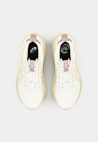 White athletic shoes with a textured upper, pink accents, and a cushioned sole. Features a black insole with a logo and light yellow outsole.