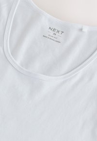 Débardeur blanc slim fit avec encolure ronde, étiqueté "NEXT M", fabriqué au Bangladesh, présenté à plat sur un fond clair.