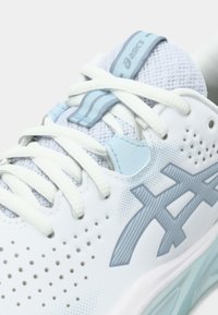 Λευκό αθλητικό παπούτσι με ανοιχτά γαλάζιες λεπτομέρειες, υφή στο πάνω μέρος, δίχτυ και οπές. Διαθέτει επίπεδα κορδόνια και εμφανές λογότυπο στο πλάι.