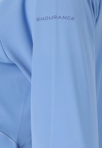 Hellblaues Longsleeve-Oberteil mit glatter Textur und tailliertem Design. Mit dem Aufdruck "ENDURANCE" auf dem Ärmel in kontrastierender Farbe.