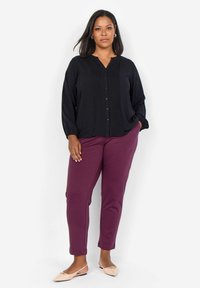 Blusa nera con bottoni e pieghe, abbinata a pantaloni slim-fit bordeaux e ballerine rosa chiaro, caratterizzata da una vestibilità rilassata e una morbida texture del tessuto.