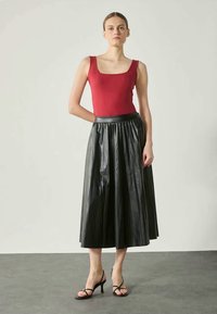 Rød, tætsiddende tanktop parret med en sort, højhalset, plisseret lædernederdel. Sorte, strapsandaler fuldender outfittet.