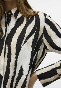 Katoenen shirt met een zwart-beige abstract streep patroon, kraag en knoopsluiting. Getextureerde stof met zichtbare stiksels.