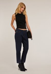 Haut sans manches noir avec une texture côtelée, assorti à un jean taille haute bleu foncé. Modèle portant des bottines noires à talons aigus et tenant un petit sac.