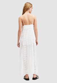 Weißes, ärmelloses Maxikleid mit Spitzenakzenten und fließendem Schnitt. Verfügt über dünne Träger und einen mittleren Rückenausschnitt. Kombiniert mit schwarzen Sandalen.