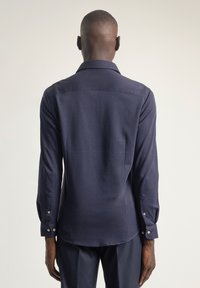 Camisa azul marino de manga larga, tejido suave, cuello clásico, puños con botones, corte entallado, canesú trasero, brillo sutil y diseño liso.