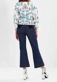 Kuvioitu monivärinen pusero puffihihnoilla, yhdistettynä tummiin farkkuleggingseihin. Hopeiset lohkossa korkeat nilkkasaappaat korostavat ilmettä.