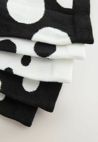 Czarno-białe skarpetki z dużymi wzorami w kropki. Tekstura materiału jest miękka i dziana. Ułożenie pokazuje jedną czarną skarpetkę na dole.