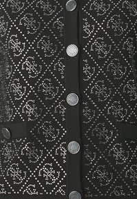 Cardigan noir à boutons sur le devant avec des embellissements en rhinestones en motif de losanges. Comprend des boutons ronds et deux poches avant.