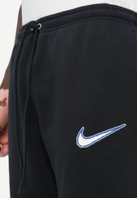 Zwarte sweatpants van zacht materiaal met een elastische tailleband, voorzien van een Nike-logo in wit en blauw op de linkerdij.