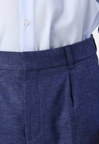 Blå linnbyxor med en strukturerad väv, med platt framdel, sidofickor och midjeband med bältesöglor. Klassisk design nära. 