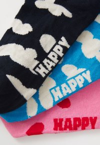 Trois chaussettes : une noire avec un motif de nuages blancs et "HEUREUX", une bleu clair avec des nuages blancs et "HEUREUX", et une rose avec des cœurs rouges et "HEUREUX".