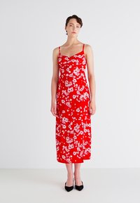 Rød blomsterkjole i midi-lengde med tynne stropper, tettsittende bodice, flytende skjørt og et lett, glatt stoff. Har et lite hvitt blomster mønster.