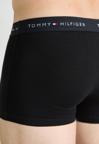 Fekete pamut boxer alsónadrág, márkás elasztikus derékkal, amelyen a "TOMMY HILFIGER" felirat és piros-fehér díszítések találhatók, sima textúrával.