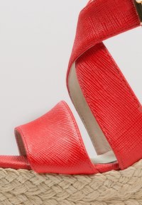 Infradito sintetici rossi con finitura testurizzata, dotati di ampie cinghie incrociate e una suola piatta in juta intrecciata.