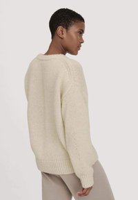 Crème-kleurige gebreide trui met een losse pasvorm, geribbelde zoom en raglanmouwen. Zachte textuur met een licht verhoogd steekpatroon.