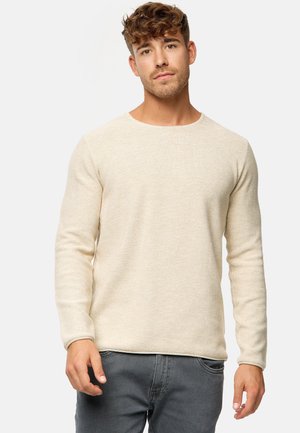 Beige knit sweater with a crew neck, long sleeves, and a textured fabric. Paired with gray jeans for a casual look.