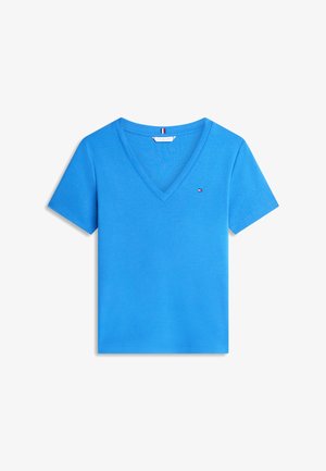 Blaues T-Shirt mit kurzen Ärmeln und V-Ausschnitt, mit kleinem roten, weißen und blauen Logo auf der linken Brust und Flaggen-Detail im Krageninnneren.