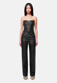 Schwarzes Leder-Corsagentop mit geschnürter Vorderseite, kombiniert mit hoch taillierter schwarzer Lederhose mit weitem Bein. Glatte Textur, minimale Details.