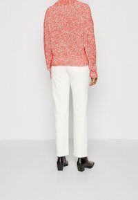 Béžový a červený pletený svetr s vysokým límcem, spárovaný s upnutými bílými džíny a černými botami na blokovém podpatku.