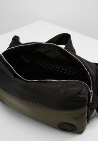 Borsa in nylon nera e verde oliva con una grande apertura con cerniera, dotata di una tasca interna con cerniera, un esterno texturizzato e un'accademia rotonda.