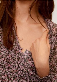 Blumige Bluse mit V-Ausschnitt-Design, auf dunklem Hintergrund mit kleinen lila und rosa Blumen, aus weichem Stoff und mit Knopfdetails.